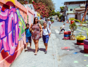 mulher com duas crianças caminha em calçada passando por muro com grafite