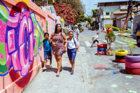 mulher com duas crianças caminha em calçada passando por muro com grafite