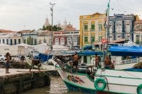 A foto mostra pesadores dentro do barco com prédios históricos ao fundo.
