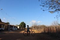 Imagem mostra mulher em uma bicicleta e, ao fundo, paisagem de Caatinga