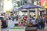 foto de uma rua em São José dos Campos. Pessoas conversam sentadas sob ombrelones na calçada. Carros passam lentamente na rua.
