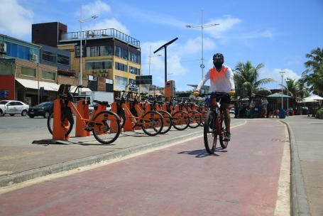 homem pedala em ciclovia ao lado de estação de compartilhamento de bicicletas