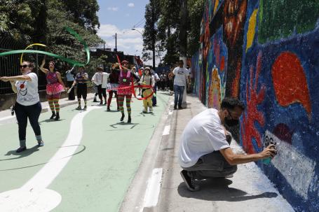 homem pinta muro enquanto pessoas passam por rua colorida