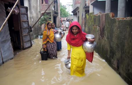 pessoas carregam pertences durante enchente em Bangladesh