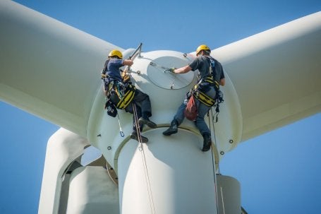 Foto mostra técnicos realizando manutenção em uma turbina eólica de grande porte
