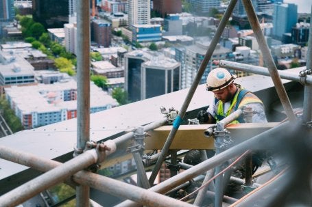 Imagem mostra homem trabalhando na construção um prédio, cercado de estruturas de metal