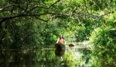 indígena navengando em barco em meio à floresta amazônica