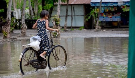 Menina pedala bicicleta em área alagada