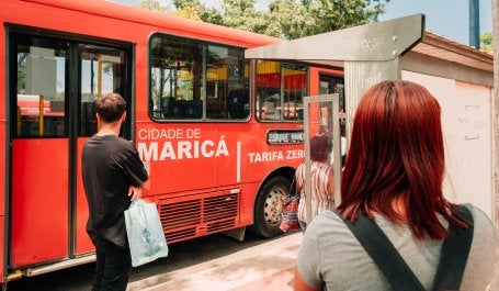 pessoas em ponto de ônibus e ônibus parado com escrito tarifa zero na lateral