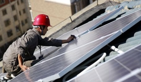 Técnico instala painel solar no telhado de um edifício na China, com céu claro ao fundo