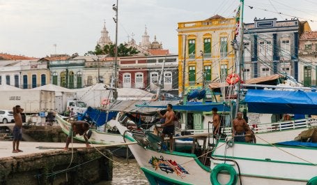 A foto mostra pesadores dentro do barco com prédios históricos ao fundo.