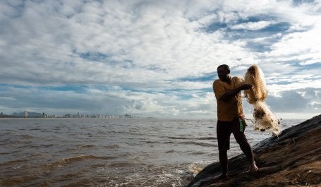 Imagem mostra pescador negro se preparando para lança a rede de pesca