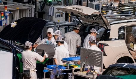 Foto mostra trabalhadores em uma fábrica de carros