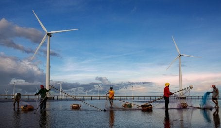 Pescadores arrumam redes em frente a estrutura de energia eólica