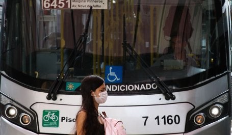 mulher da máscara passa em frente a ônibus